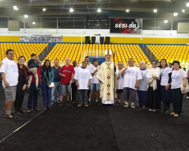 Descrição da imagem: fotografia do bispo Dom Luiz Carlos Dias que se encontra ao centro de um grupo de aproximadamente vinte pessoas, entre homens, mulheres e uma criança no colo. Ao fundo é possível observar uma arquibancada com bancos amarelo. Fim da descrição. Descrição da imagem: fotografia do bispo Dom Luiz Carlos Dias que se encontra ao centro de um grupo de aproximadamente vinte pessoas, entre homens, mulheres e uma criança no colo. Ao fundo é possível observar uma arquibancada com bancos amarelo. Fim da descrição.